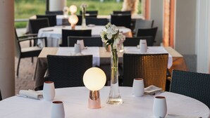 Un espace de restauration en plein air avec des tables rondes, des nappes blanches et des chaises en osier.
