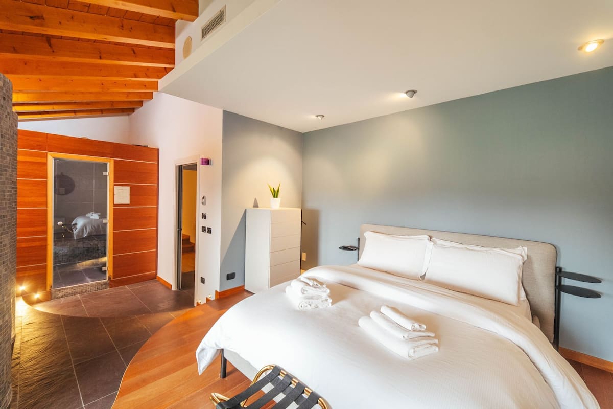 Ein modernes Hotelzimmer mit Holzboden, einem großen Bett mit weißen Bettwäsche, einem kleinen Nachttisch und Blick auf einen Balkon.