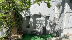 Ein Innenhof mit grünem Kunstrasen, einer Sitzgelegenheit im Freien mit Metallstühlen und -tischen sowie einer Steintreppe.