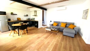 Ein zeitgemäßer Wohnraum mit Essbereich, grauem Sofa mit orangenen Kissen und einer Küche im Hintergrund.