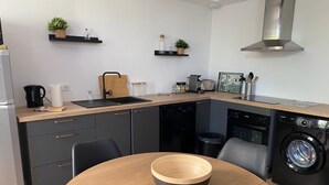 Eine moderne Küche mit einem runden Holztisch, eingebautem Geschirrspüler, Waschmaschine und einer Edelstahl-Dunstabzugshaube.