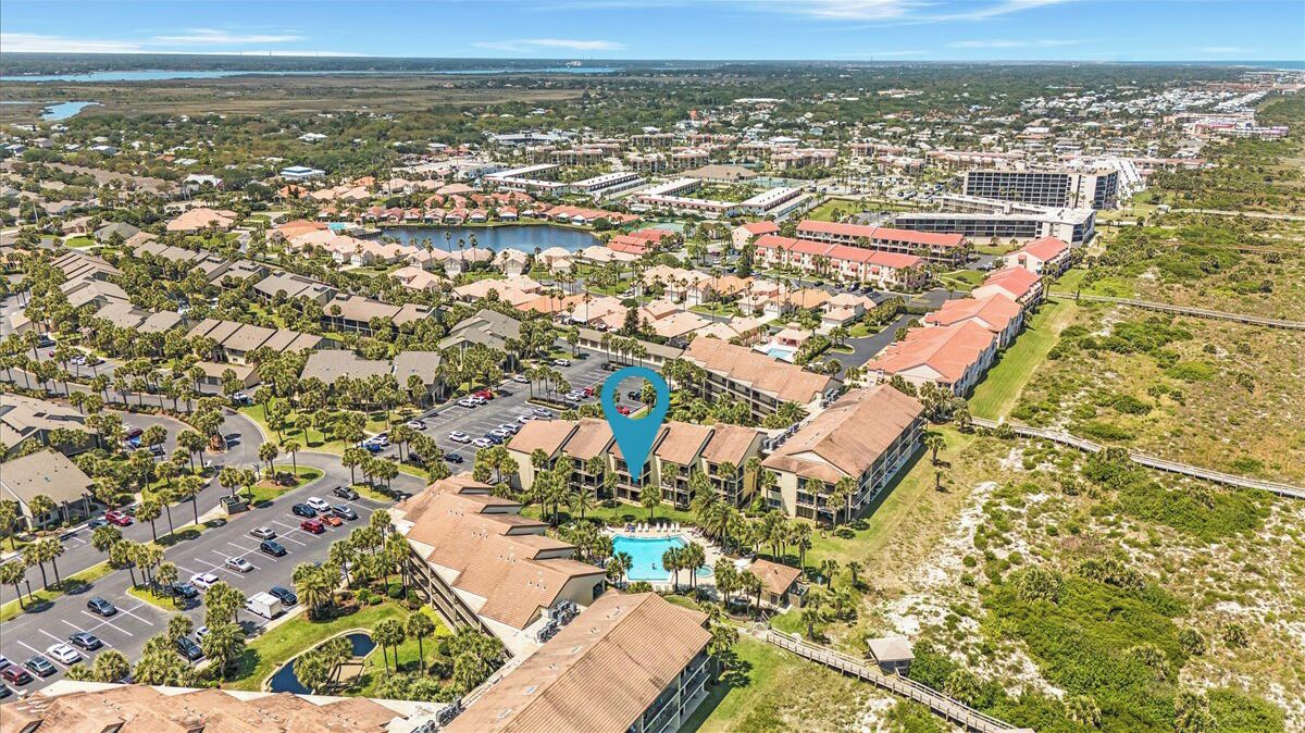 An aerial view of a resort area with multiple buildings, a central swimming pool, and surrounding greenery.