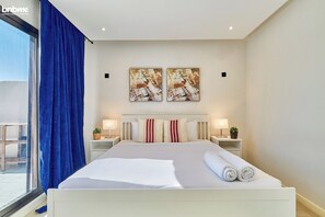 A hotel room with a large bed, two bedside tables with lamps, a window with blue curtains, and two abstract paintings on the wall. - bnbmehomes-2BR nr Boulevard City-D13 (Riyadh)
