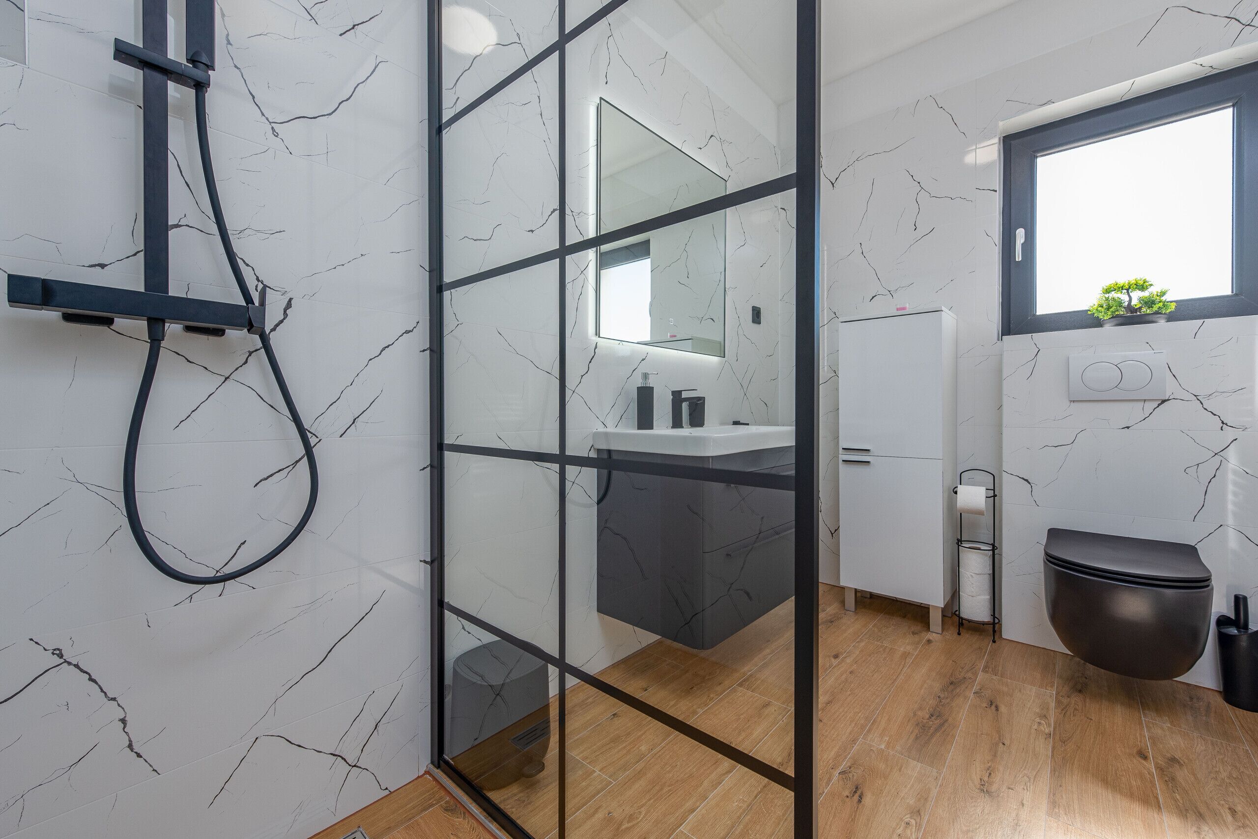 A modern bathroom with a glass partition, a shower, a sink, and a toilet.