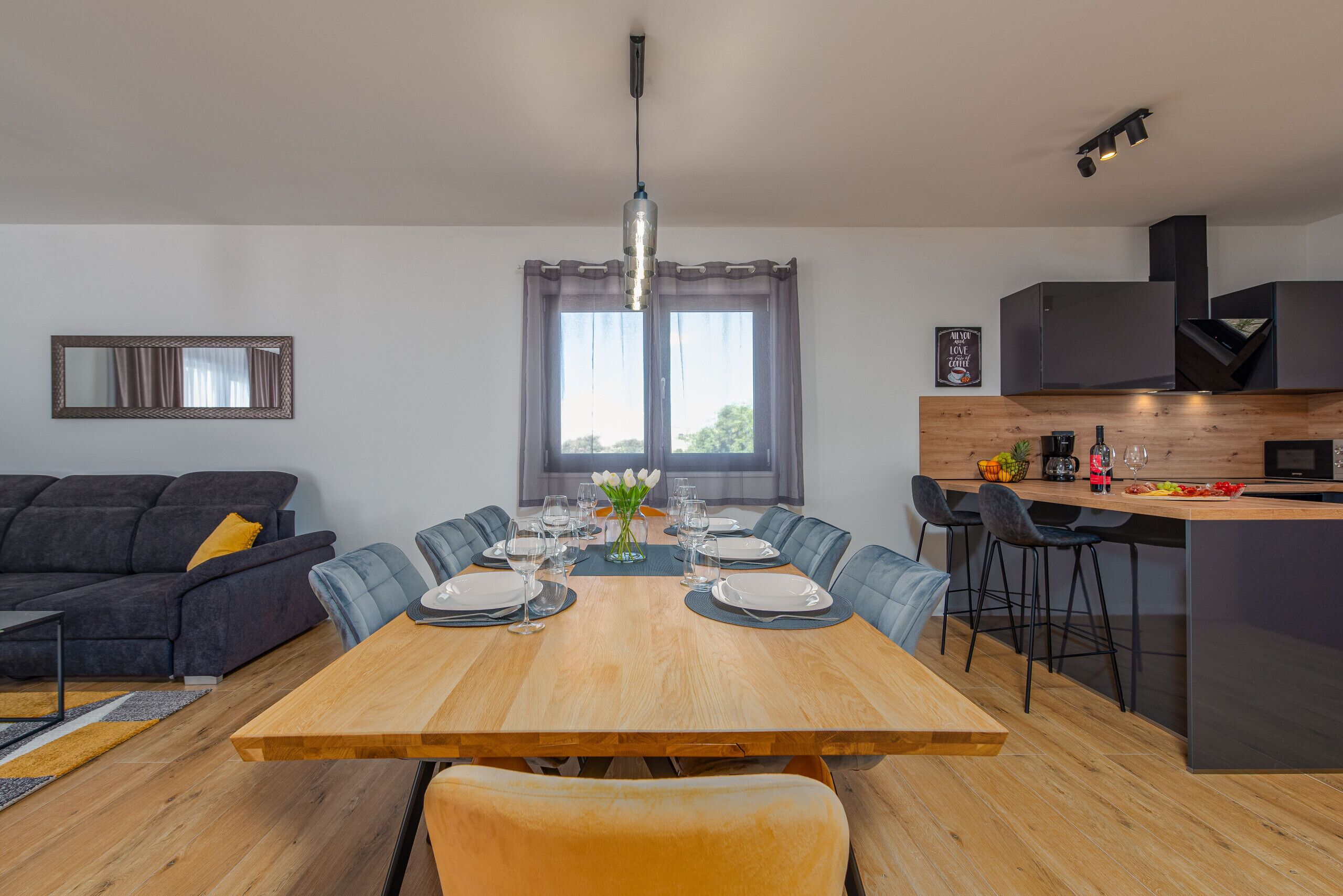 A modern kitchen with a wooden island, bar stools, and a dining table set for six.