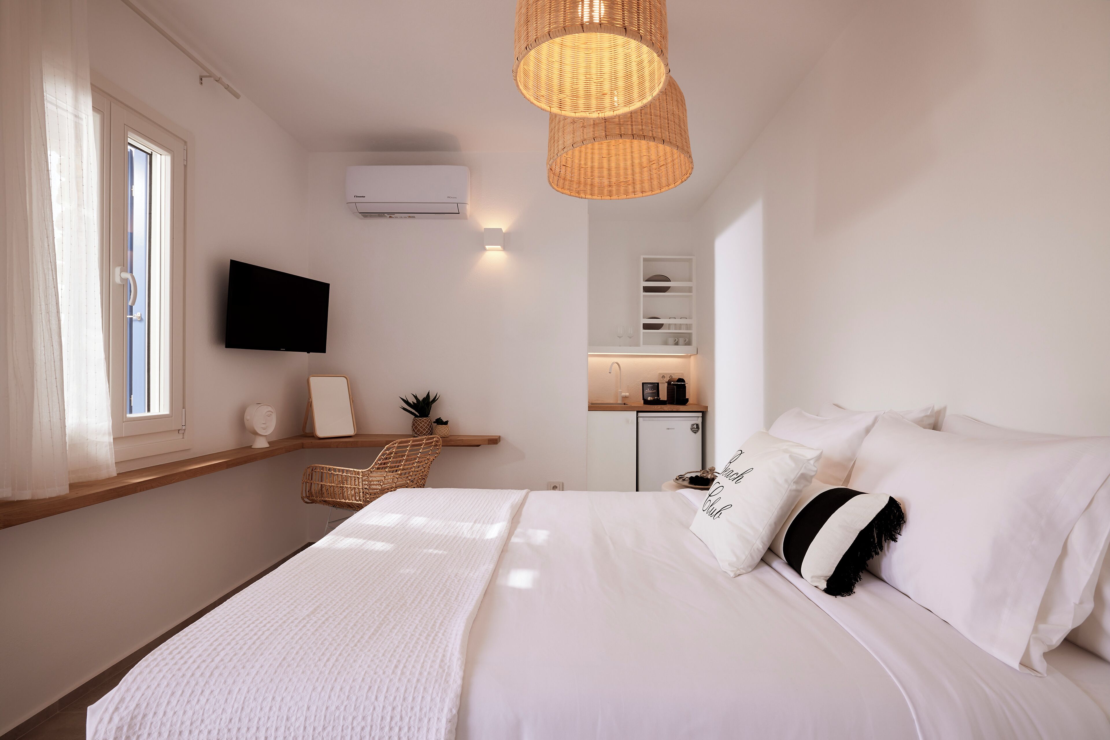 A bedroom with a bed, a television, a small kitchenette, and a window with curtains.