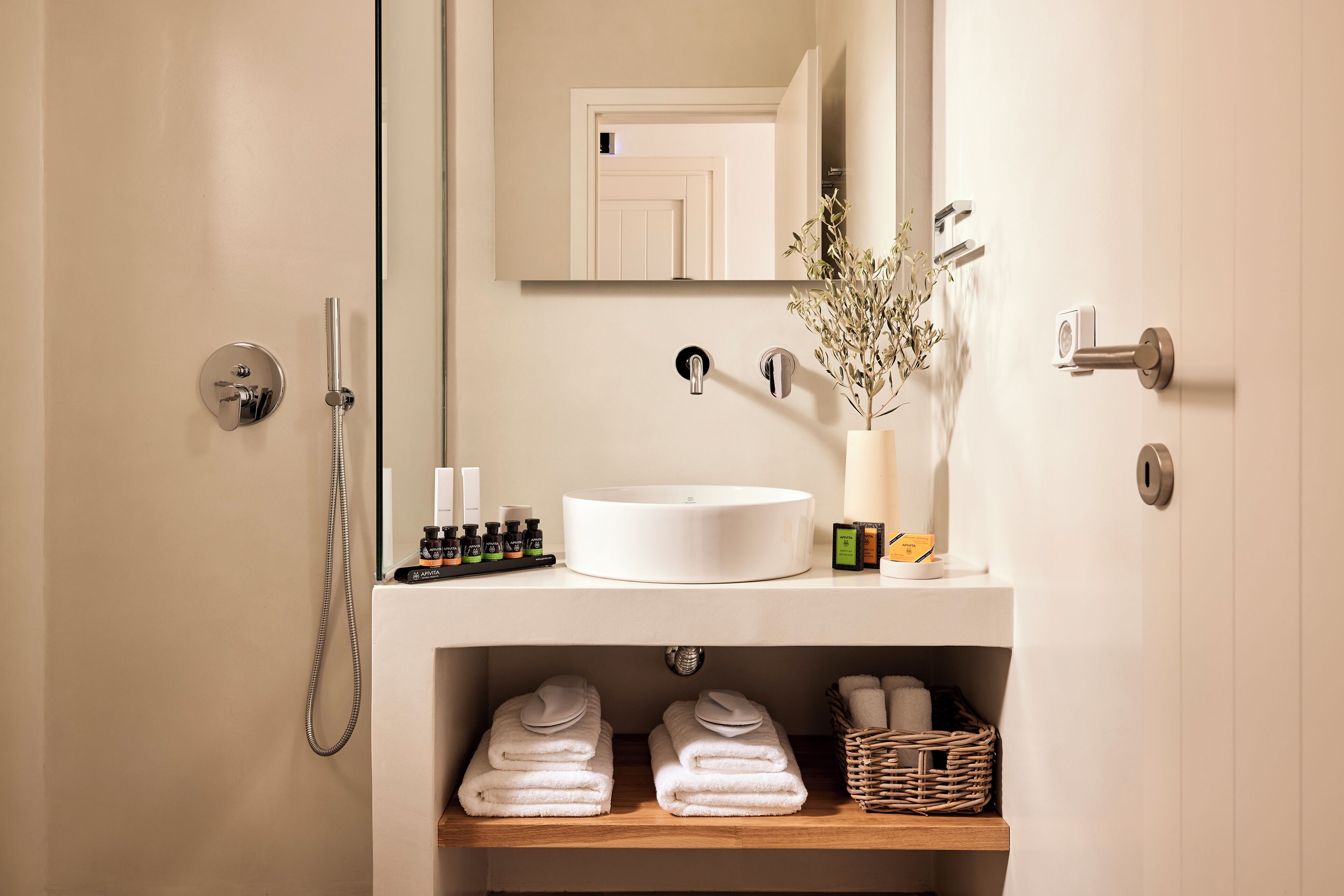 A bathroom with a white sink, a mirror, a shower, and a shelf with towels and toiletries.