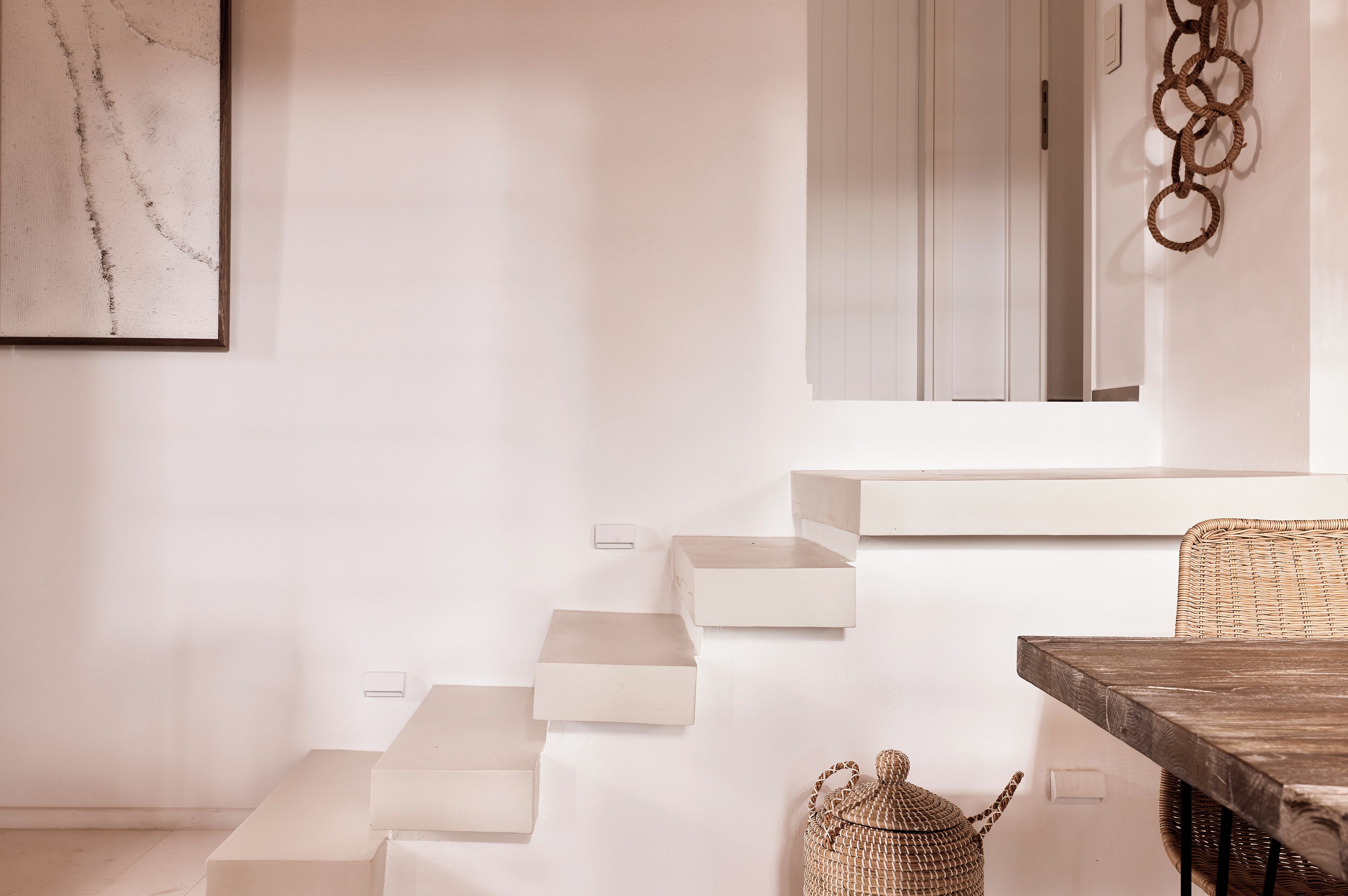 A minimalist interior with a staircase, a dining table, and a wicker basket.