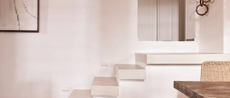 A minimalist interior with a staircase, a dining table, and a wicker basket.