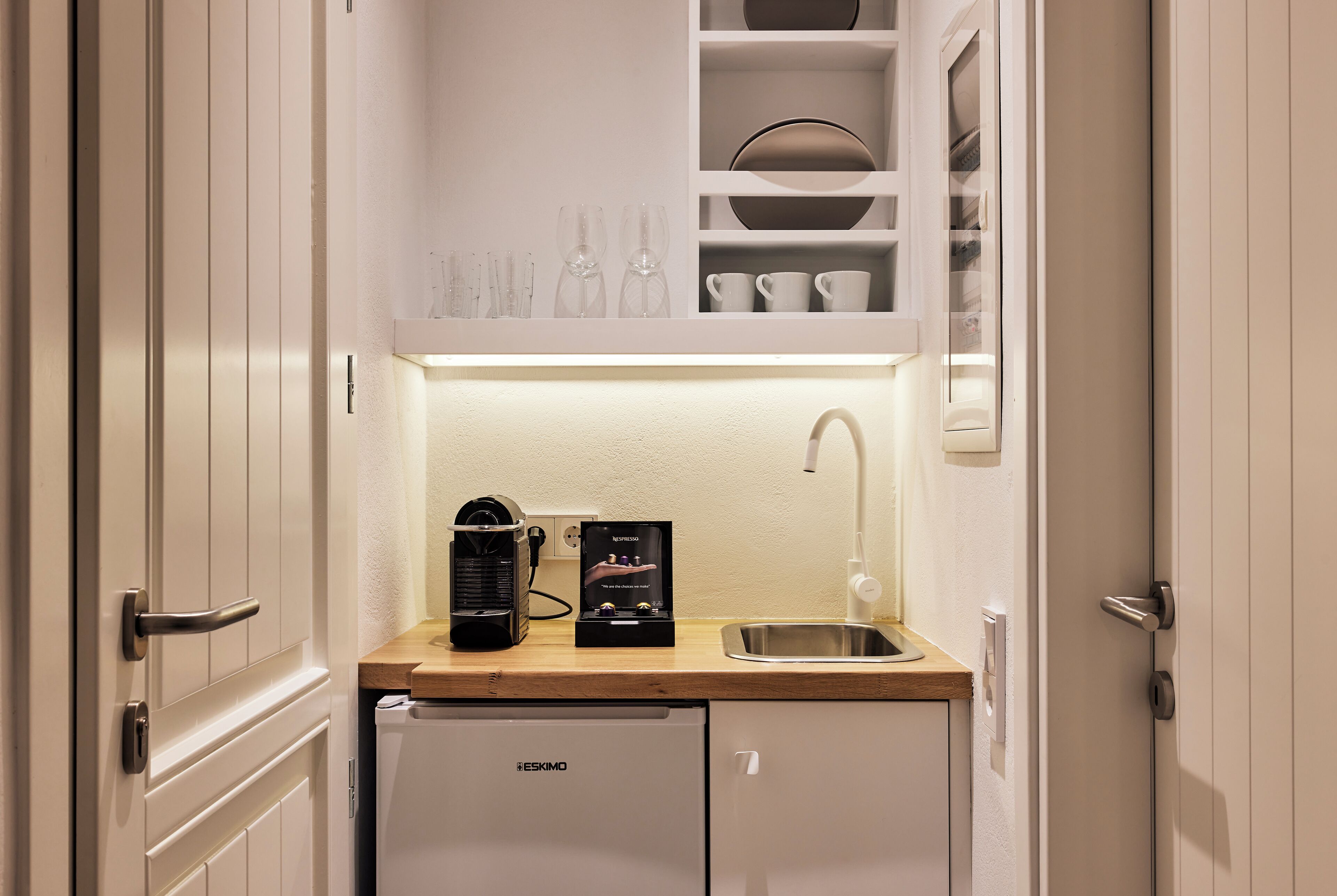 A compact kitchenette with a built-in coffee maker, a sink, and a small refrigerator.