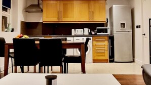 A compact kitchen with wooden cabinets, a microwave, a refrigerator, and a dining table with chairs. - Private Garden Flat Central London Air Conditioning (London)