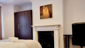 A bedroom with a bed, a dark wardrobe, a painting above a fireplace, and a chair. - Private Garden Flat Central London Air Conditioning (London)