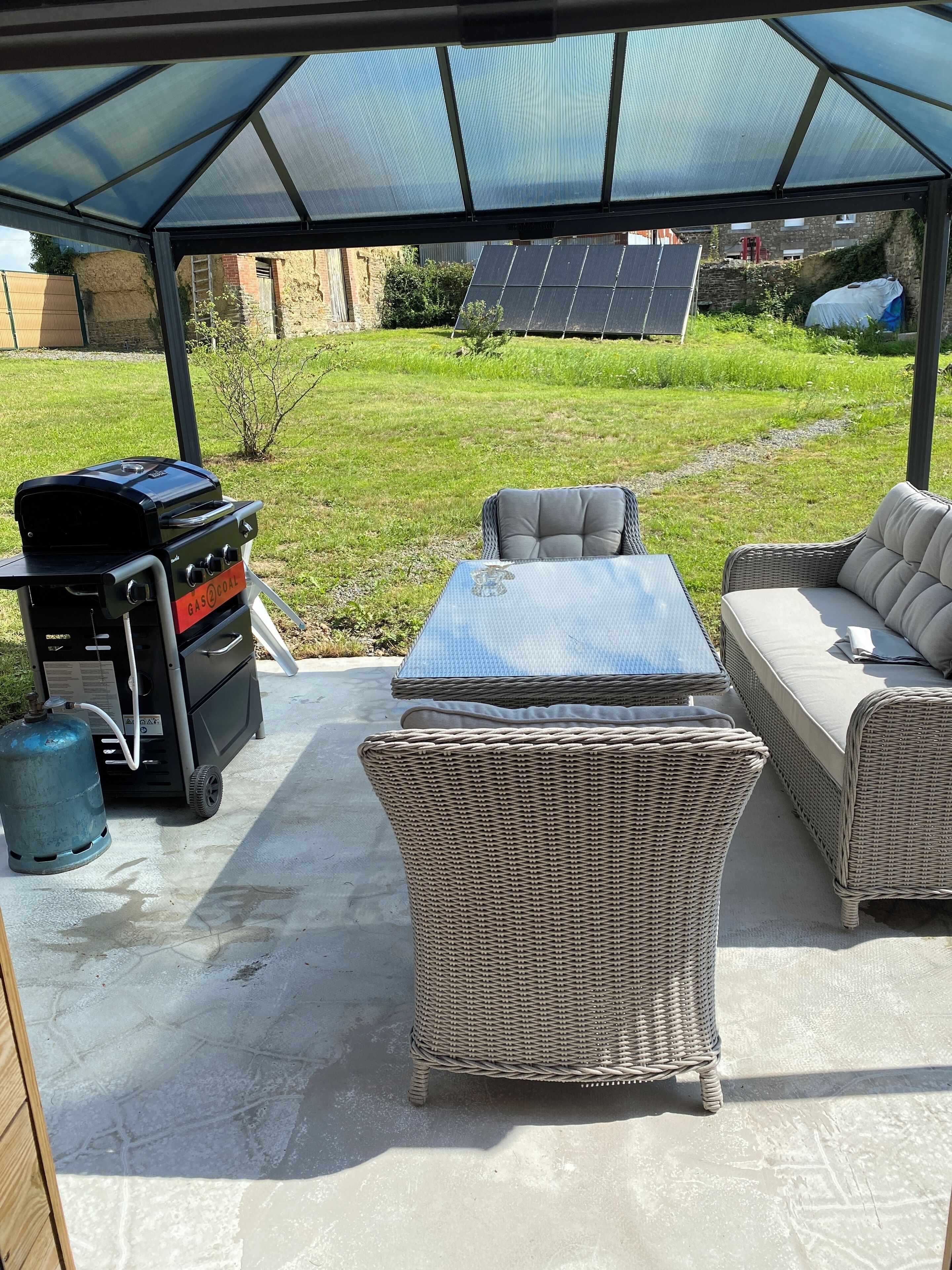 Un patio couvert aménagé avec du mobilier d’extérieur, un barbecue et une bouteille de gaz.