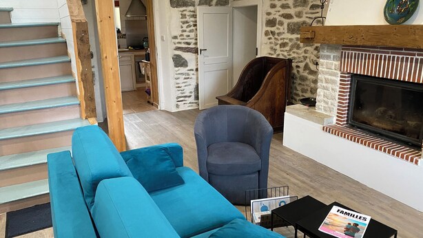 A living room with a blue sofa, a dark armchair, a fireplace, and a magazine on a small table.