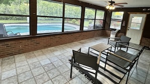 A covered patio area with brick walls, large windows, and ceiling fans.
