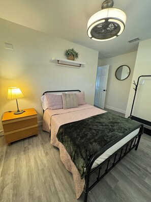 A bedroom with a bed, bedside table, lamp, shelf with a plant, and a round mirror on the wall. - Gorgeous pool home in South Lakeland. Family and pet friendly! (Lakeland)