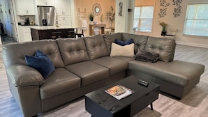 A modern living room with a sectional sofa, a coffee table, and a kitchen in the background.
