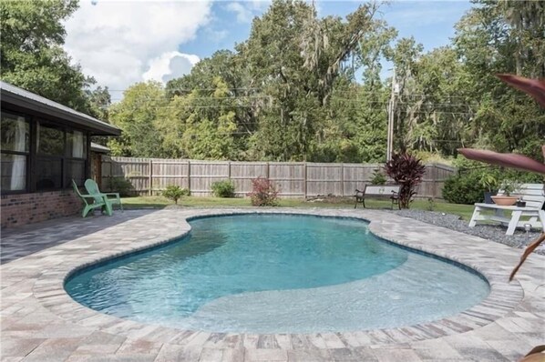 A swimming pool with a curved edge, surrounded by a stone deck. There are two green chairs and a small table near the pool. - Gorgeous pool home in South Lakeland. Family and pet friendly! (Lakeland)