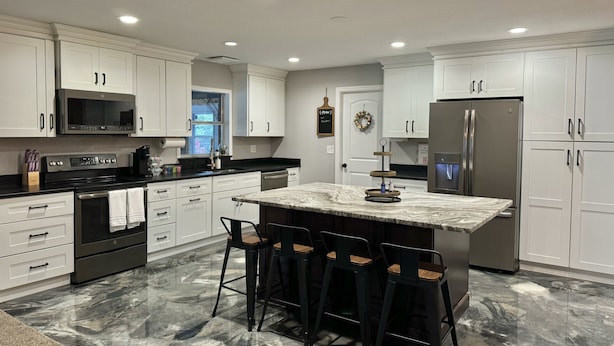 A modern kitchen with white cabinets, a stainless steel refrigerator, a black countertop, and a marble island with bar stools.