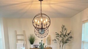 A dining room with a wooden table, white chairs, a chandelier, and decorative plants.