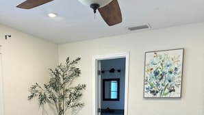 A bedroom with a bed, a ceiling fan, a potted plant, and a bathroom visible through an open door.