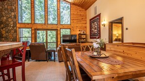 A spacious dining area with a wooden table and chairs, a television, and a stone wall. - Millville Chalet ~ Pool Access! (Camp Connell)