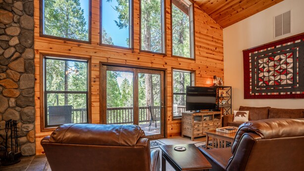 A cozy cabin interior with a stone fireplace, leather seating, a TV, and a quilted wall hanging. - Millville Chalet ~ Pool Access! (Camp Connell)