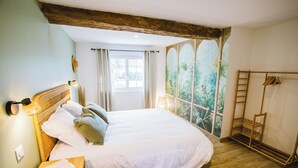Un dormitorio con una cama grande, cabecera de madera, mesita de noche con un libro, ventana con cortinas y vista a zonas verdes.