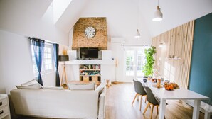 Una sala de estar moderna con una cama entrepiso, un comedor con mesa y sillas, una chimenea de ladrillo y un ventanal con cortinas.