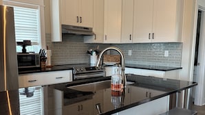 A modern kitchen with white cabinets, a black countertop, and a central island with bar stools. - “Sound Decision” Carova Beach Canal Front Home!! 4x4 Required (Corolla)