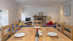 A dining area with a wooden table set for four, a bottle of wine, and a stone fireplace in the background.