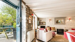 A cozy living room with a stone wall, white furniture, a fireplace, and a view of the outdoors. - 1 Penally Boathouse Mews, Holiday Cottage St Dogmaels, Sleeps 4, 2 bedrooms,  bathrooms (Cardigan)
