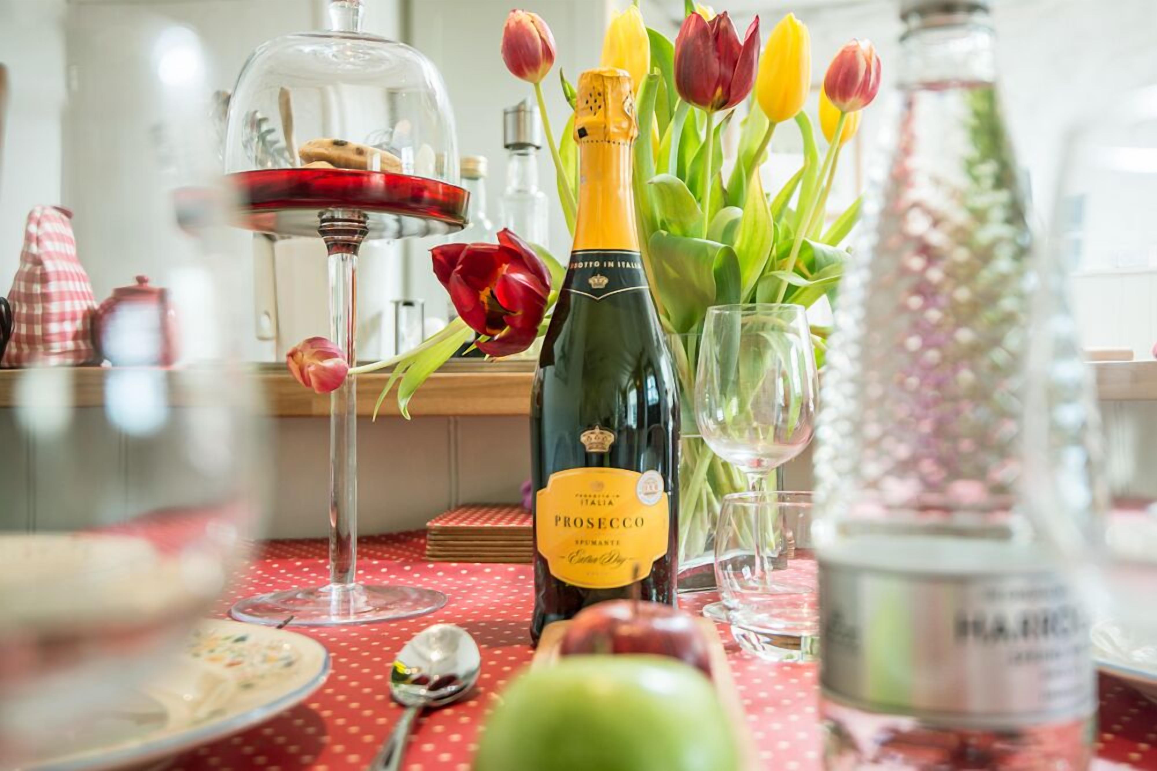 Een eettafel met een fles Prosecco, tulpen en een wijnglas.
