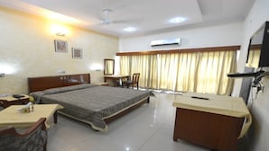 A hotel room with a bed, a desk, a chair, a sofa, and a TV. - Aravalli Golf Course (Faridabad)