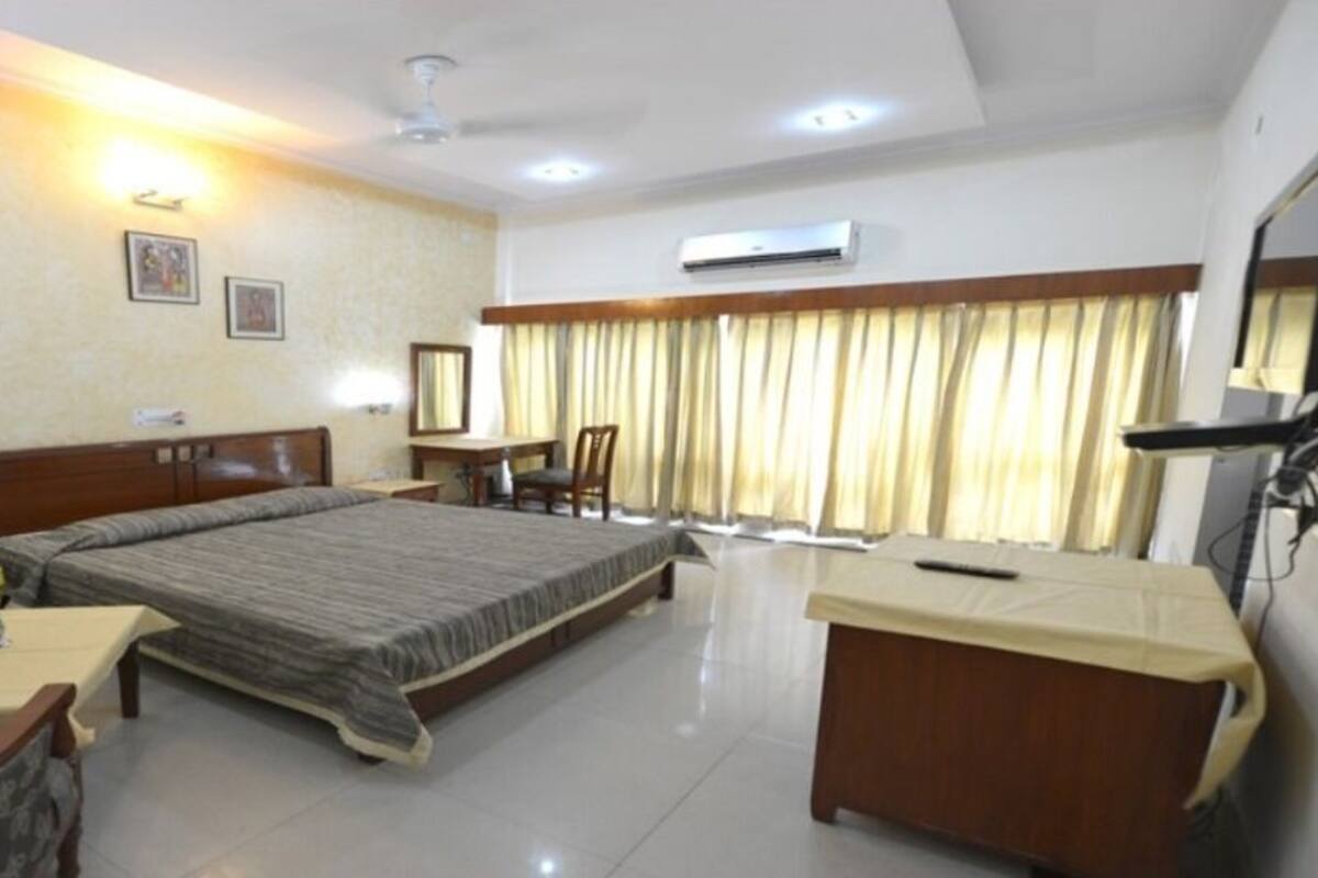 A hotel room with a bed, a desk, a chair, a sofa, and a TV.