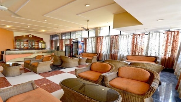 A lobby with wicker furniture, a checkered floor, and a reception area with a counter and display cases. - Aravalli Golf Course (Faridabad)