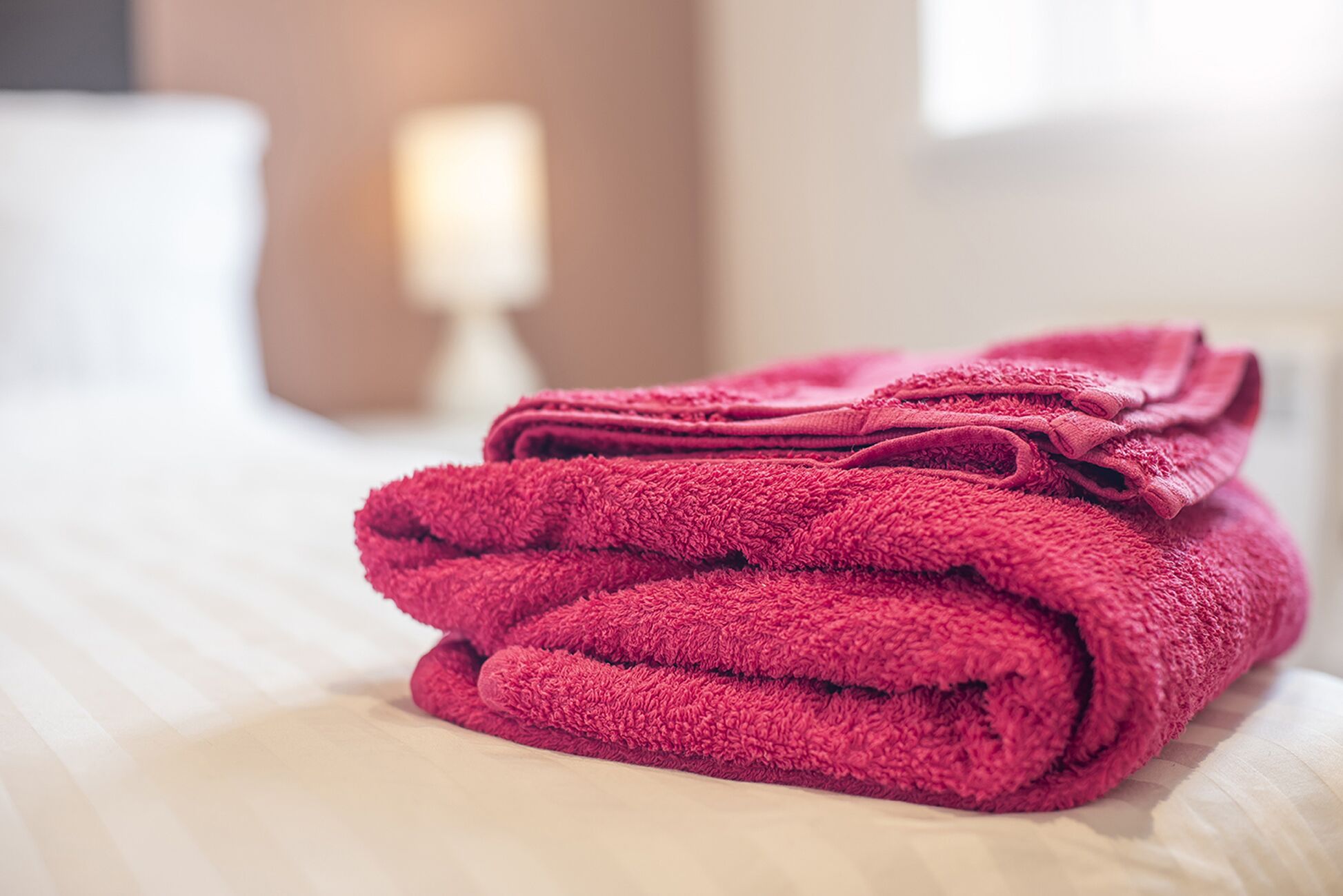 Ein ordentlich gefalteter Stapel roter Handtücher auf einem Bett mit weißer Bettwäsche.