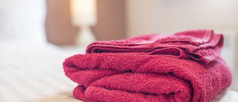 A neatly folded stack of red towels on a bed with a white sheet.