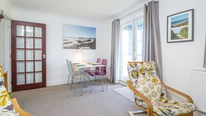 Et værelse med en trædør, et spisebord med farverige stole, en blomstret lænestol og et stort vindue med gardiner.