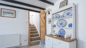 A room with a white radiator, a wooden staircase, a white cabinet with blue and white plates, and a framed picture on the wall. - 15 Newport Road, Holiday Cottage Fishguard, Sleeps 5, 3 bedrooms,  bathrooms (FISHGUARD)