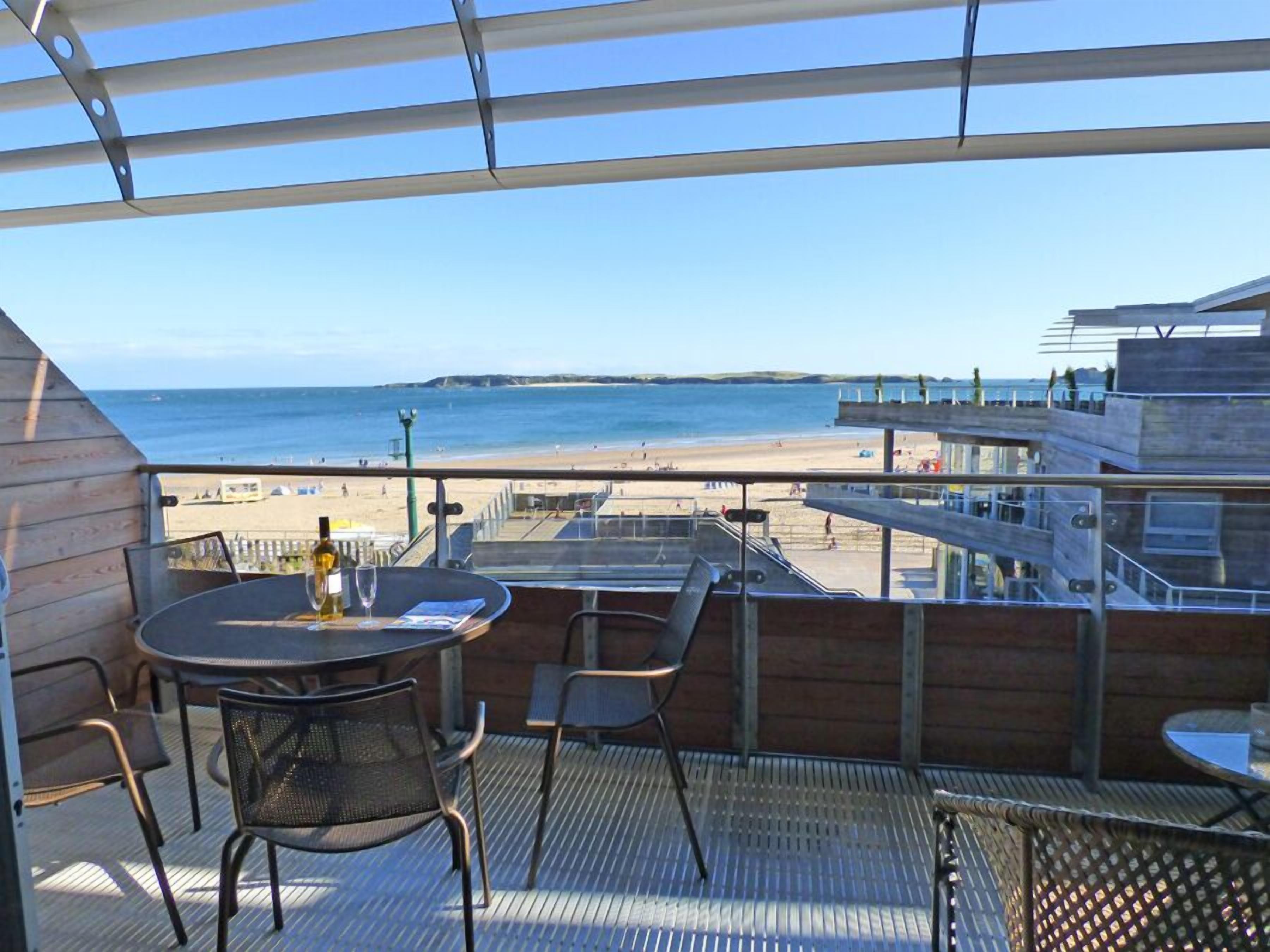 Un balcón con vistas a la playa, una mesa con sillas y una botella de vino.