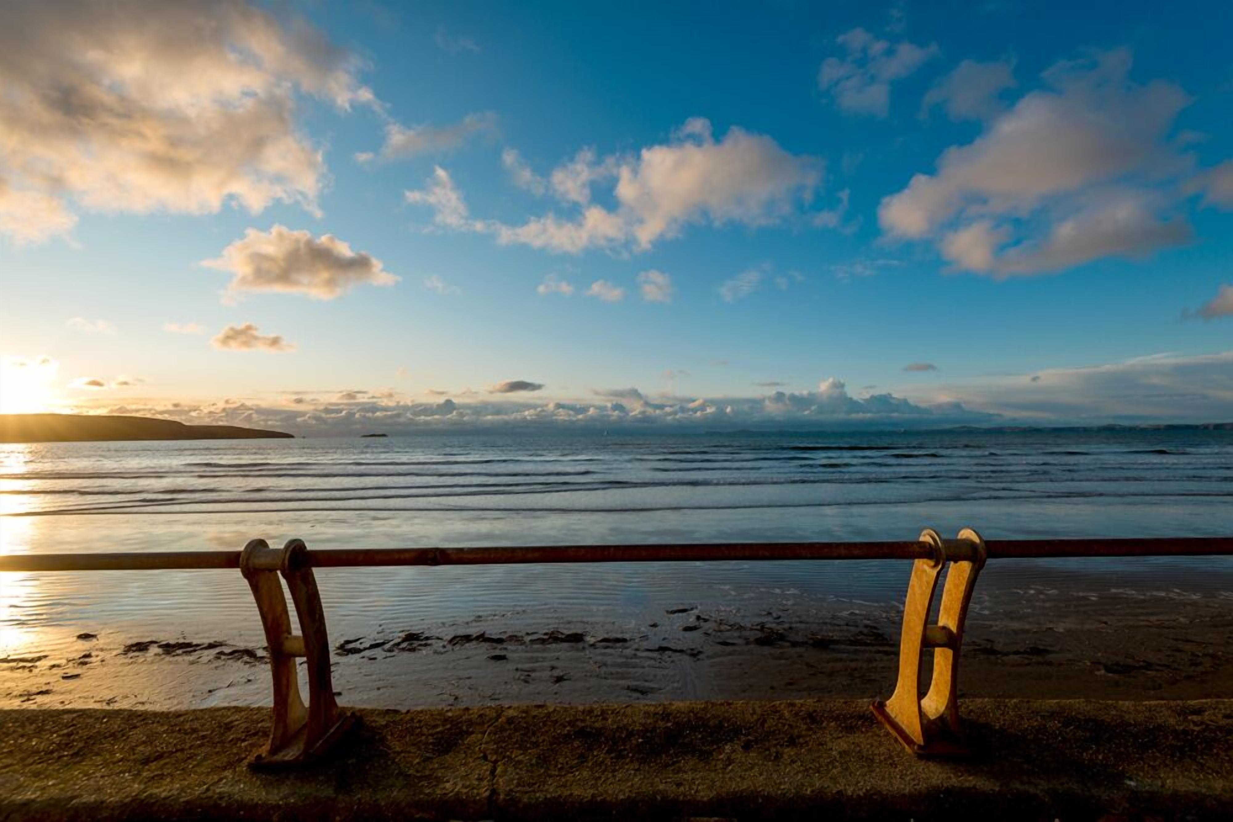 A beach with a wooden railing and a sunset in the background.