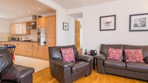 A modern living room with leather sofas, a dining area with a blue chair, and a kitchen with wooden cabinets. - 2 Coastal View, Holiday Home Llanunwas, Solva, Sleeps 2, 1 bedrooms,  bathrooms (Haverfordwest)