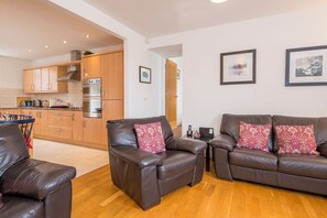 A modern living room with leather sofas, a dining area with a blue chair, and a kitchen with wooden cabinets. - 2 Coastal View, Holiday Home Llanunwas, Solva, Sleeps 2, 1 bedrooms,  bathrooms (Haverfordwest)