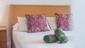 A neatly made bed with striped bedding and two patterned pillows, a wooden headboard, and a wooden nightstand with a drawer. - 2 Coastal View, Holiday Home Llanunwas, Solva, Sleeps 2, 1 bedrooms,  bathrooms (Haverfordwest)