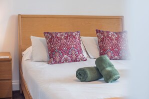 A neatly made bed with striped bedding and two patterned pillows, a wooden headboard, and a wooden nightstand with a drawer. - 2 Coastal View, Holiday Home Llanunwas, Solva, Sleeps 2, 1 bedrooms,  bathrooms (Haverfordwest)