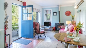 Ein gemütliches Wohnzimmer mit Kamin, einem Essbereich mit Tisch für Zwei und einer blauen Tür, die zu einem Außenbereich führt.