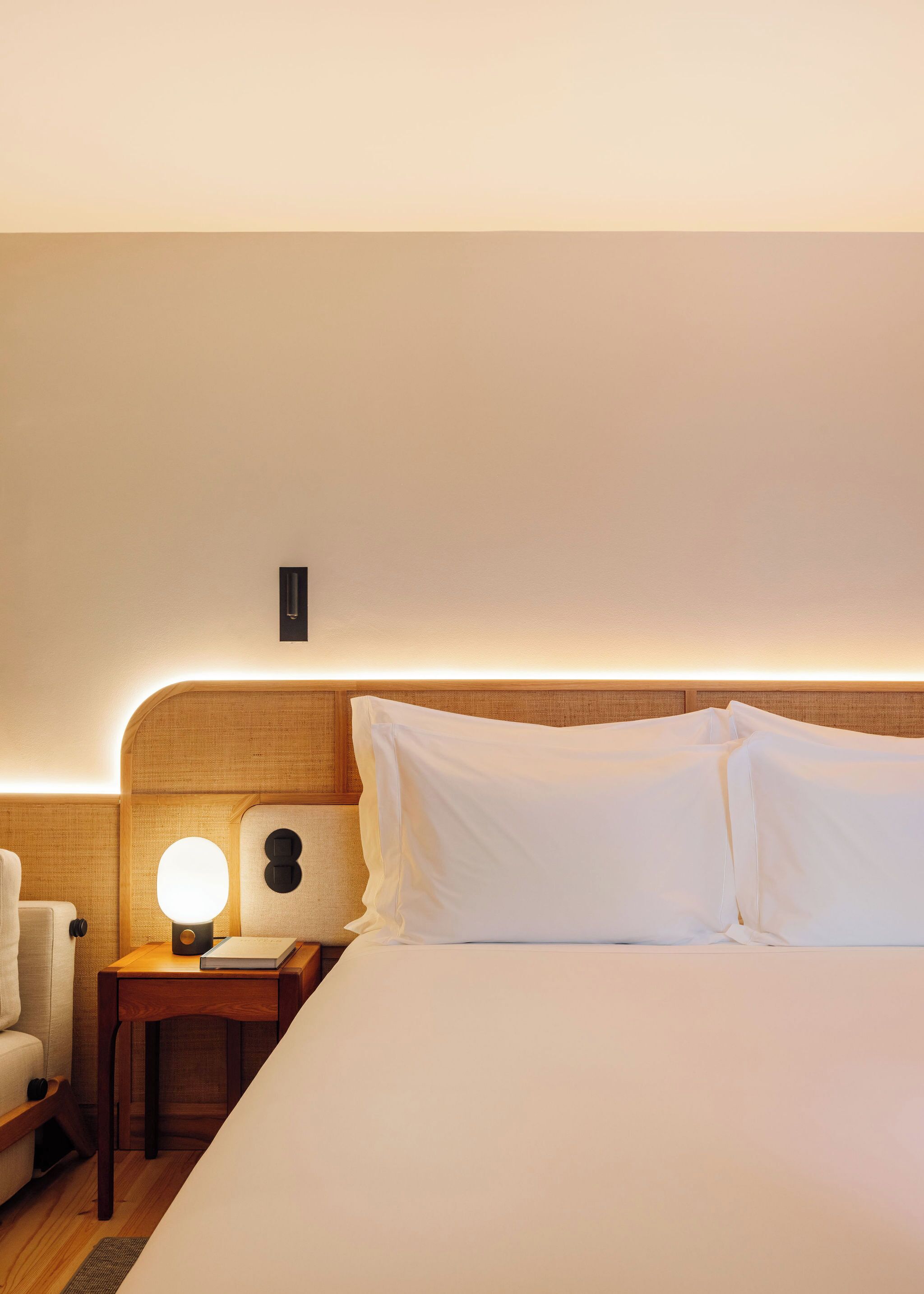 Una habitación de hotel con una cama bien hecha, una mesita de noche con una lámpara y una silla.