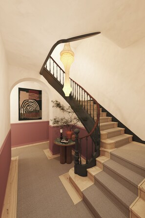 A staircase with a wooden handrail and a black railing, leading to a landing with a potted plant and a wall-mounted artwork. - The Verse (Lisbon)