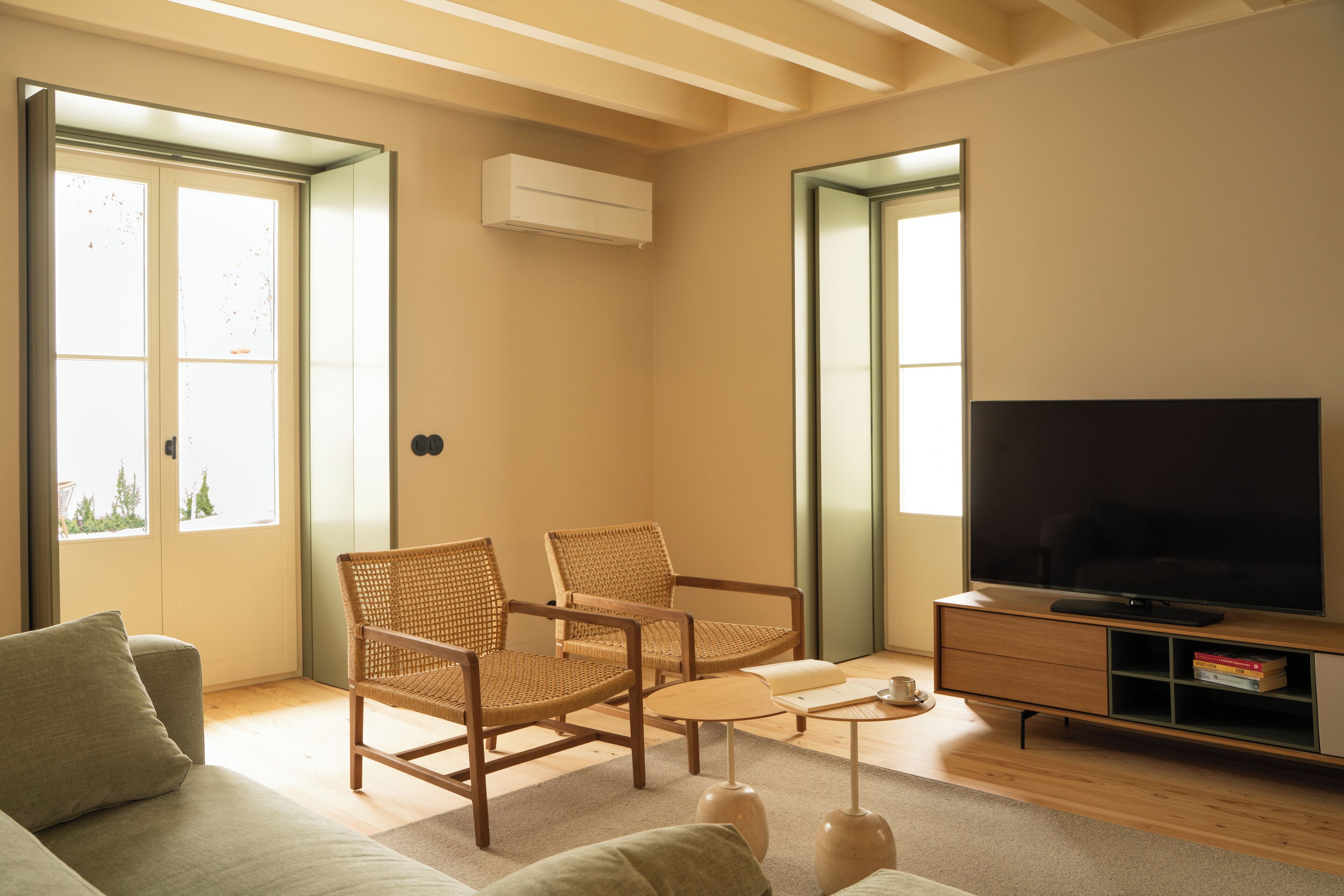 A modern living room with a sofa, two wicker chairs, a coffee table, a TV on a wooden stand, and a bookshelf.